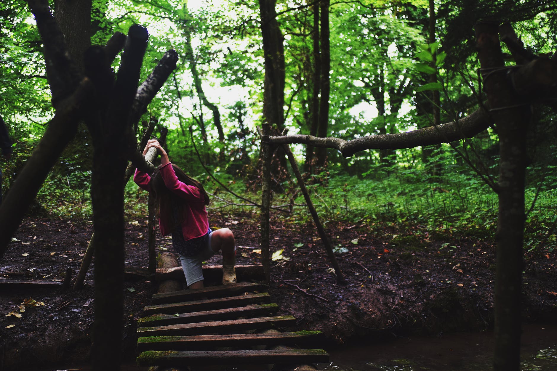 girl in pink jacket on wooden bridge in the forest